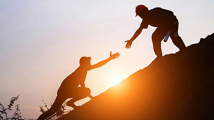 Foto de un hombre acercándose a otro para ayudarlo a subir una colina