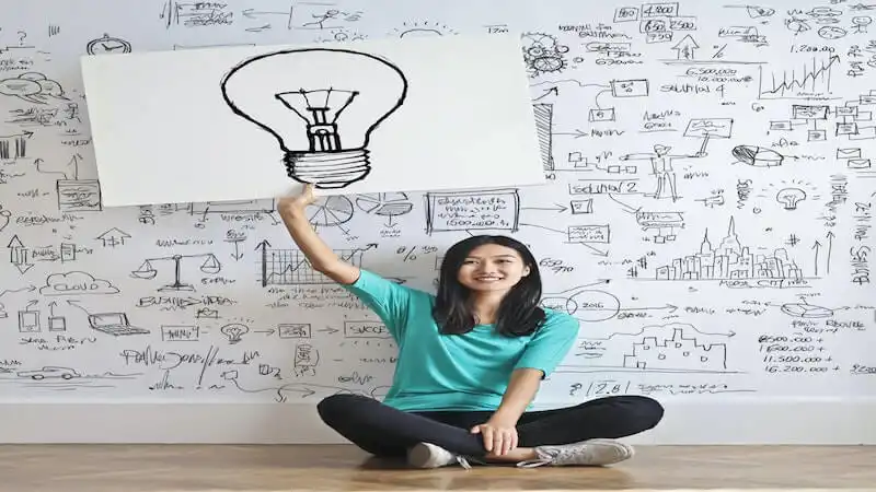 The image shows a girl sitting on the floor holding a poster with a lamp.