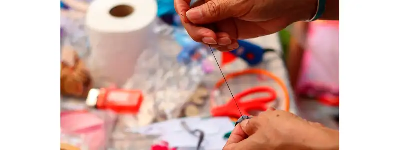 6 mãos de uma mulher produzindo um artesanato com fios