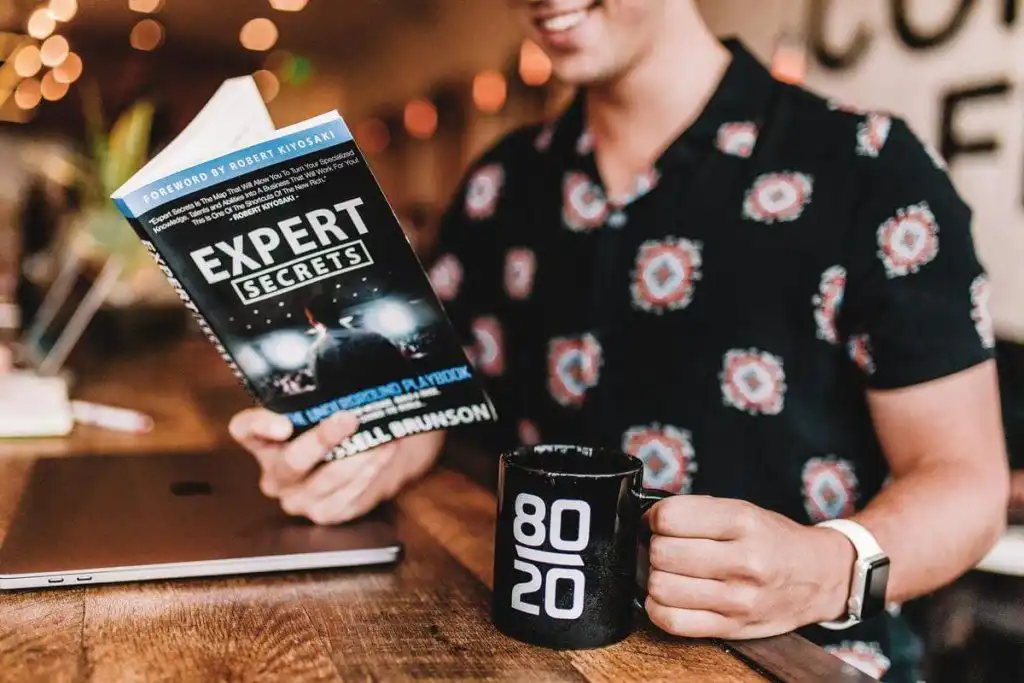 Hombre leyendo libro con el título "Expert Secrets"