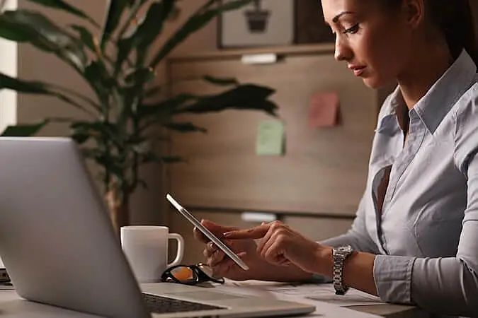 Real estate agent working at desk using laptop and smartphone to respond to client inquiries quickly