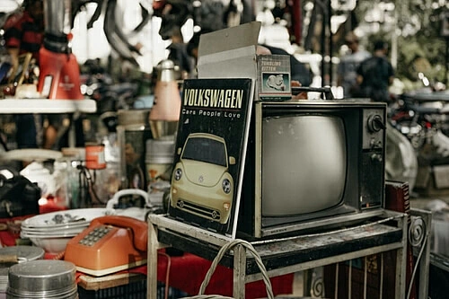 The image shows a garage sale, there are various products on d a table, including a TV and a telephone.