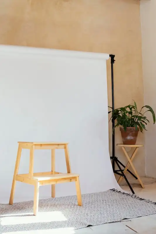 How to take product photos - white backdrop Whte backdrop, and in front of it there is a small stool, on the right side is a plant vase on a table.