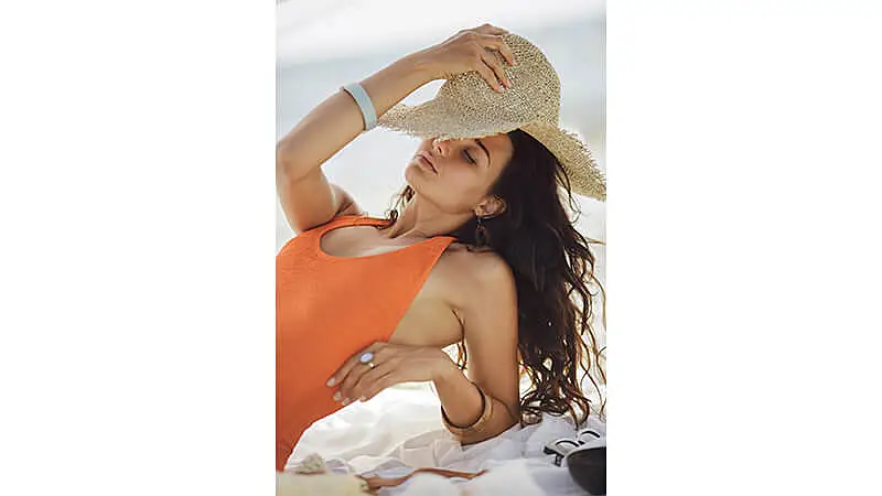 Foto de uma mulher na praia segurando o chapéu