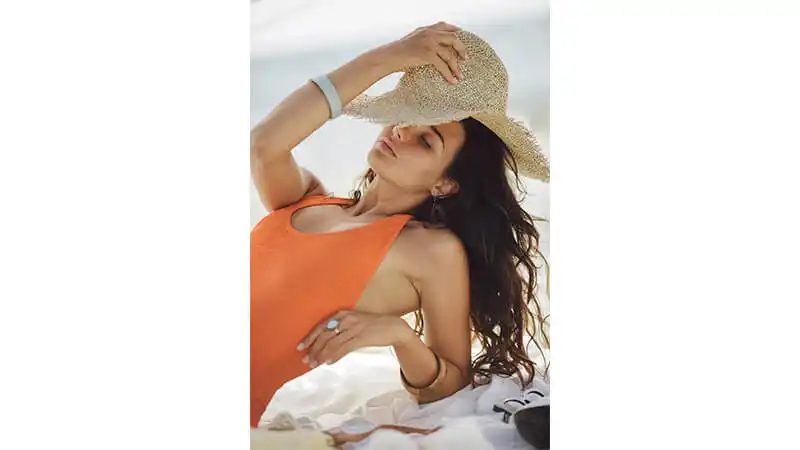 Foto de uma mulher na praia segurando o chapéu