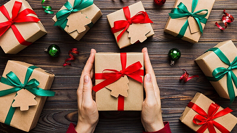 Imagem de duas mão segurando um presente com laço e várias caixas de presente