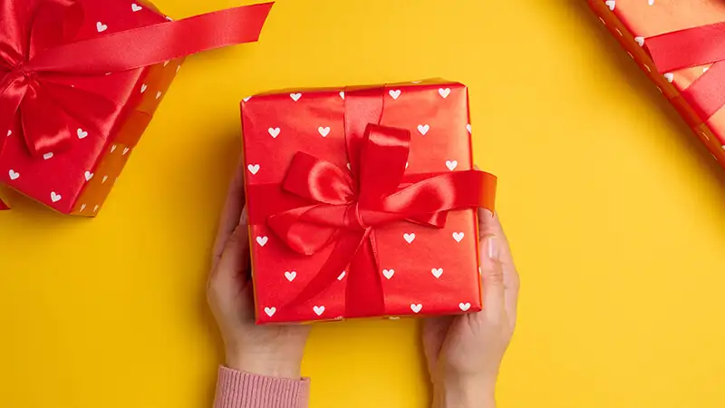 Imagem de duas mãos segurando uma caixa com laço