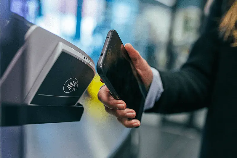 The image shows a person aproximating a smartphone to a payment machine.