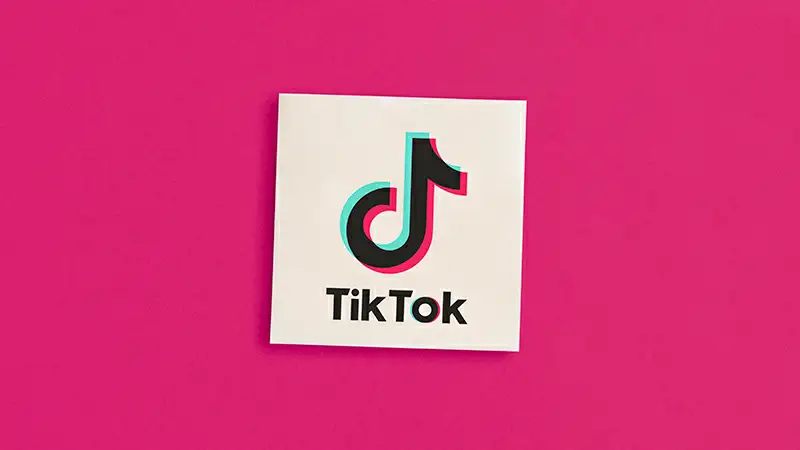Melhor horário para postar Tik Tok Ilustração de uma pessoa sentada e um celular com a logo do TikTok