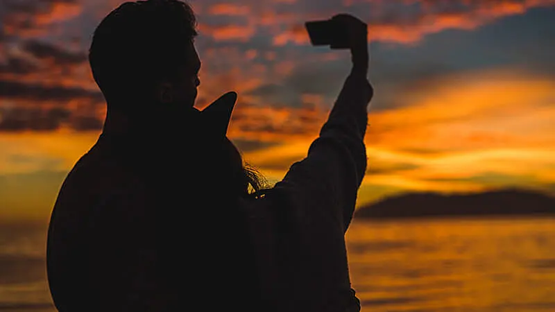 Foto da silhueta de um homem tirando foto de um pássaro voando com o por do sol ao fundo
