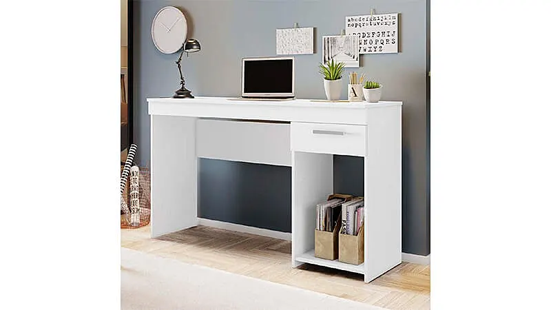 imagem de uma mesa para escritório na cor branca com uma gaveta, com diversos objetos em cima e em uma sala com chão de madeira e parede cinza