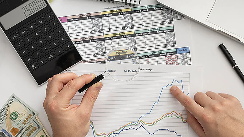 Foto de uma mesa com um notebook, notas de dinheiro, celular e papeis 