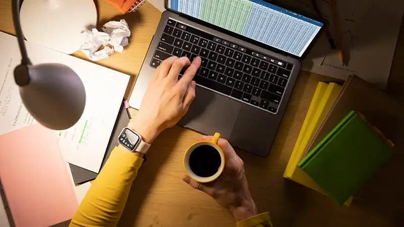 Foto de uma mulher sentada utilizando um notebook em cima de uma mesa
