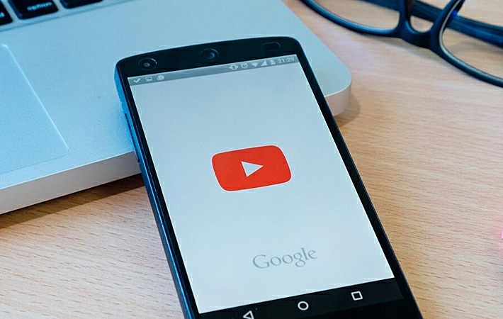 Foto de um celular com a logo do YouTube em cima de um notebook