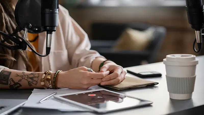 nome para podcast Foto de mãos de uma pessoa em cima de uma mesa e microfones