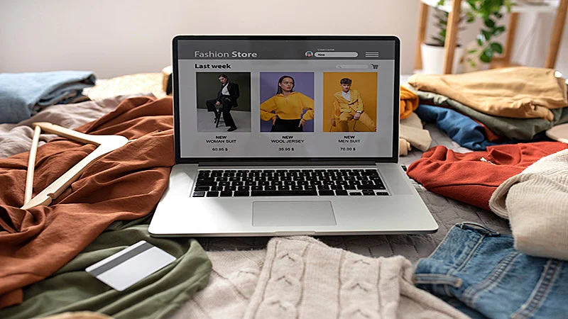 Foto de um notebook em cima da cama e várias roupas