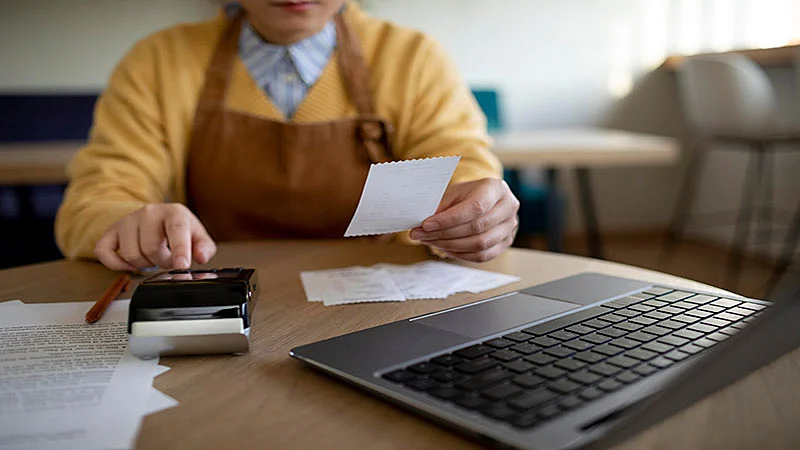 Foto de um homem analisando notas e um notebook