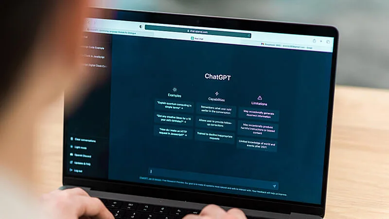 Foto de um notebook na mesa e uma mão segurando um celular aberto no ChatGPT
