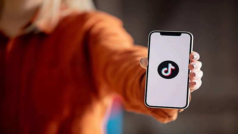 Foto de uma pessoa segurando um celular com a logo do tiktok