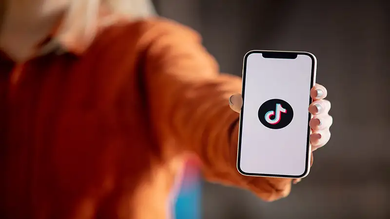 Foto de uma pessoa segurando um celular com a logo do tiktok
