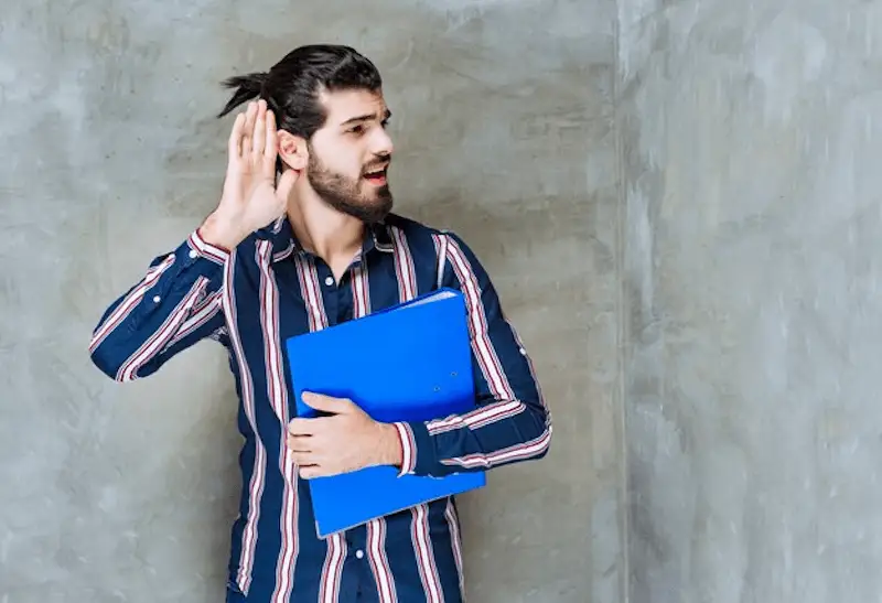 The image shows a man with a hand on his ears trying to hear something.