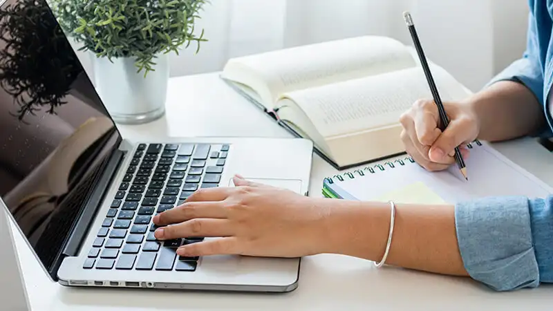 Foto de uma pessoa usando o notebook e uma agenda em cima da mesa