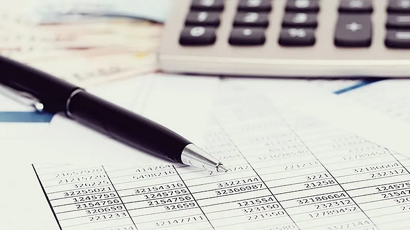 Foto de uma planilha com uma calculadora em cima e uma caneta