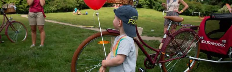 criança segurando um balão ao lado de uma bicicleta em um parque