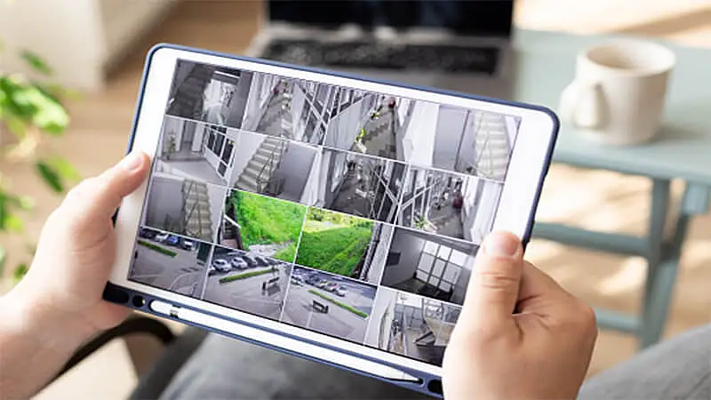 Foto de uma pessoa segurando um tablet olhando câmeras de segurança