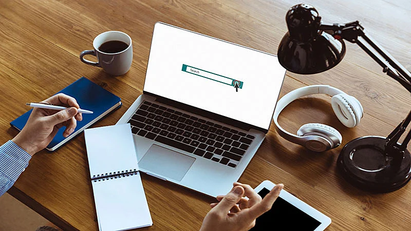 Foto de um notebook em cima da mesa e mão com uma caneta na mão