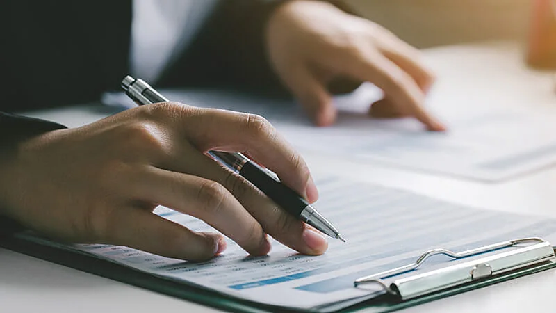 Foto de uma pessoa segurando uma prancheta com um papel e outra pessoa segurando uma caneta