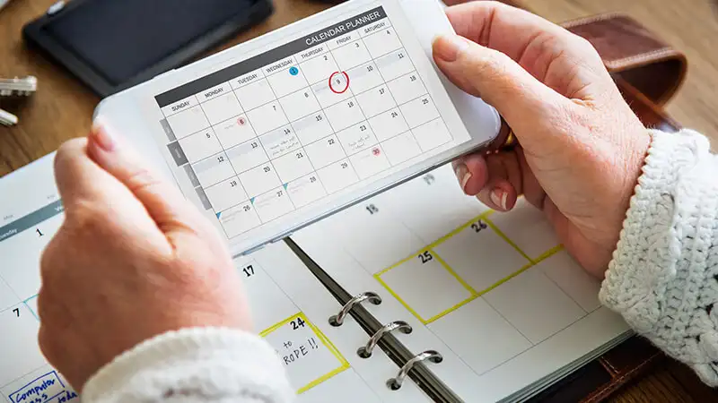 Sistema de agendamento online Imagem de uma mão segurando um celular aberto em um calendário