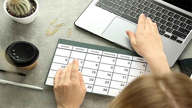 Foto de uma pessoa usando um notebook e anotando em um calendário