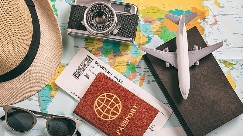 Uma foto de um óculos, uma câmera em cima de um mapa dobrado, uma mala e um avião em miniatura, todos em cima de uma mesa.