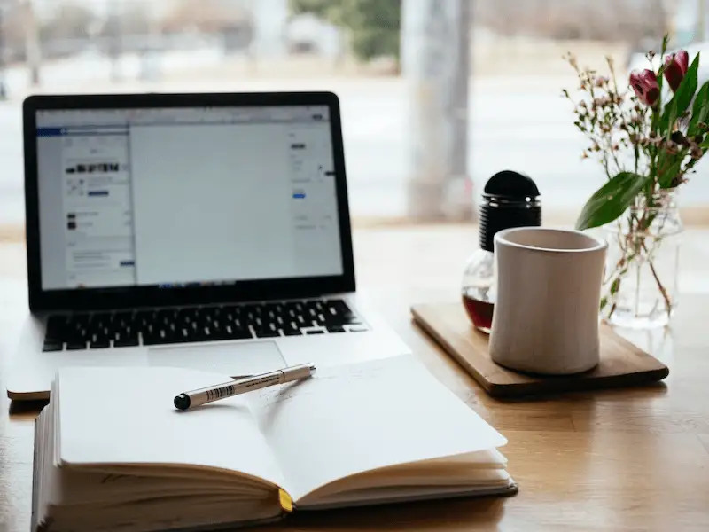 The image shows laptop and a notebook on a table.