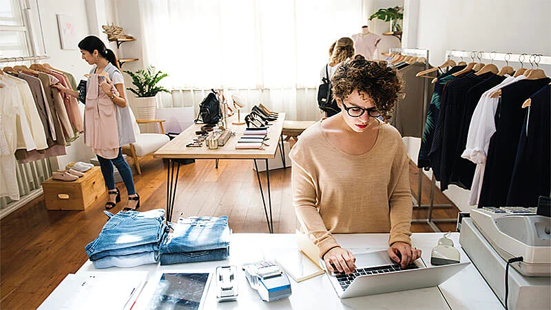 Foto de tienda de ropas con tres personas. Una trabajando en el ordenador.