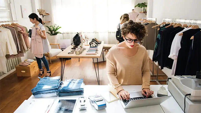 Foto de tienda de ropas con tres personas. Una trabajando en el ordenador.
