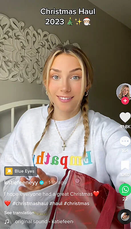 Katie Feeney is seating on her bed, and it's written "Christmas Haul 2022" on the screen.
