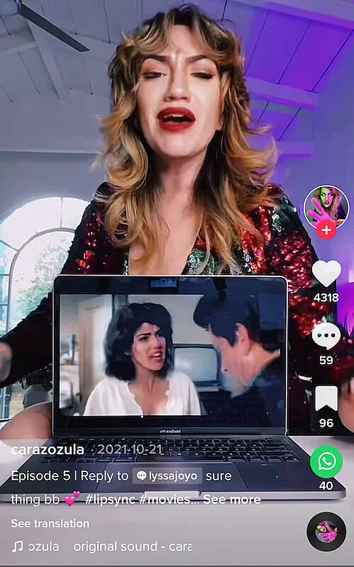 A woman is lip-syncing and in front of her there is a laptop showing the scene from a movie.