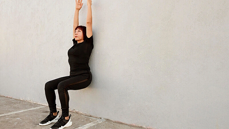 Foto de uma mulher fazendo a cadeirinha na parede em seu treino em casa