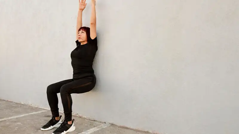 Foto de uma mulher fazendo a cadeirinha na parede em seu treino em casa