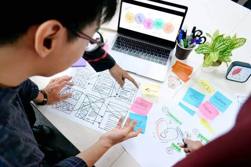 The image shows several sketches on a table and a people looking and pointing to them.