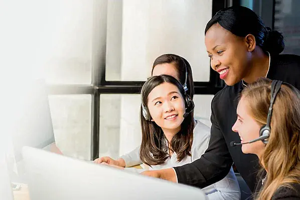 The image shows 4 women in front of computers with headsets